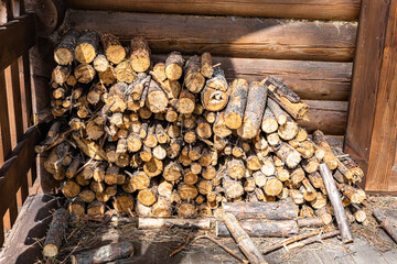 A rustic pile of stacked firewood against a log cabin wall in warm sunlight. Winter, comfort, and...