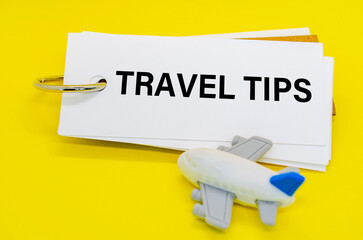 Travel Tips text on white notepad with toy airplane on yellow cover background. Away from office concept