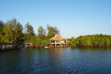 Obraz premium Peaceful waterfront house surrounded by lush greenery and calm water under clear blue sky