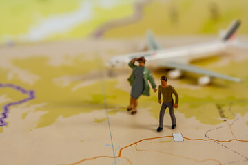 Selective focus of miniature tourist couple people walking on map with plastic toy airplane.