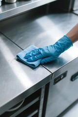 Hand wearing blue glove cleaning stainless steel surface with blue microfiber cloth
