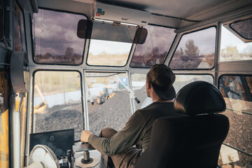 A crane operator controls heavy machinery at a coal loading dock located by the river, supervising...