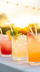 Refreshing colorful cocktails with citrus and mint served in glasses with straws on an outdoor table during a golden sunset.

