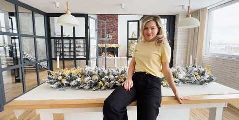 A beautiful smiling woman poses in the studio against the background of a white Christmas tree with a luminous garland.