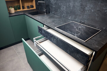 Induction cooker black tempered glass hob aspirating induction hob on marble stoneware countertop with horizontal sliding pull out drawer shelf storage in kitchen cupboard.