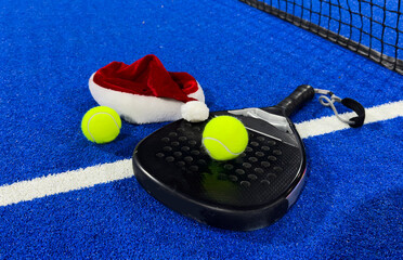 Santa Claus hat on tennis racket and ball on blue background. Merry Christmas and Happy New Year...