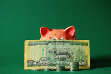 Stacks of Coins with Nepali Banknote and Piggy Bank on Green Background