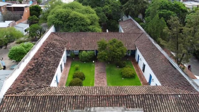 Drone flight over the colonial facade of the Casa Hist&oacute;rica de Tucum&aacute;n, its windows, flags, shields, and the lush green vegetation of its inner courtyards, including the historic well.