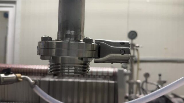 Close-up of a stainless steel industrial pipe fitting with threaded joint and hose connector, used in a pressurized liquid system or processing line.
