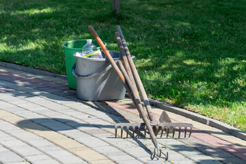 Naklejka premium Garden tools of rake hoe fork on backyard in springtime. Still life with gardening functional equipment in agriculture. Instrument diy spring work and hobby in countryside. Work tool and rural scene.