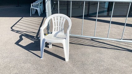 Solitary white plastic chair basking in sunlight, casting artistic shadows, perfect for Dia de la...