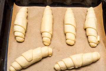 Croissant shaped dough on baking paper and baking tray, ready to bake croissants.