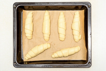 Top view of uncooked croissants on baking paper and baking sheet.