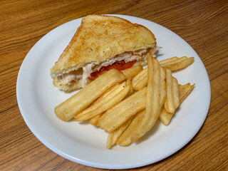 A half a club sandwich with crinkle cut fries. Half a grilled turkey sandwich with cheese bacon and tomato and fries on the side.