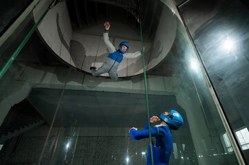 A male instructor teaches a woman how to fly in a wind tunnel. Free fall simulator.