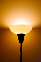Top of a floor lamp illuminating the wall in the background.