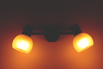 Wall lamp with two globes and two bulbs, illuminating the wall in the background.