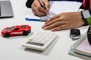 A close-up of a man’s hand signing official papers after purchasing a vehicle, reflecting the...