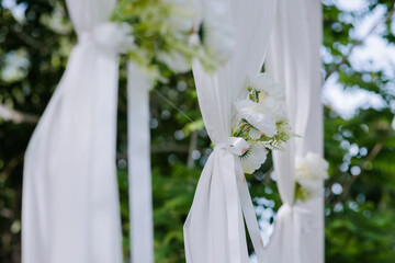 White flowers with green leaves tied together into a bouquet are attached to white cloth to decorate the wedding aisle, making it look beautiful and simple.	