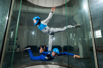 A male instructor teaches a woman how to fly in a wind tunnel. Free fall simulator.