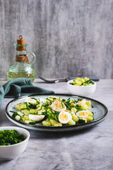 Fresh salad of cucumbers, quail eggs and green onions on a plate on the table vertical view