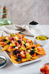 Mexican nachos chips with olives, tomatoes, salami and cheese on a plate vertical view