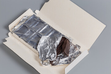 Partially broken off dark chocolate bar in open paper wrapper
