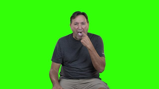 Middle-aged man reacts with visible disgust, grimacing and sticking out his tongue in a strong expression of revulsion. Isolated on green screen for easy compositing in various projects.  	