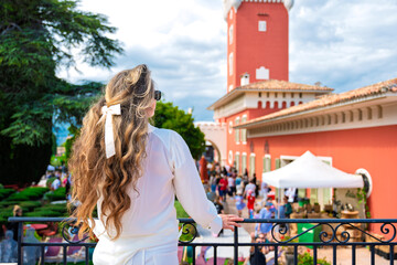 Woman posing at Chateau de Cremat with red building, and people visiting