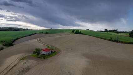 Italy, May 15, 2025: Aerial view of a farmhouse equipped with solar panels in the middle of plowed fields. Peace, tranquility with renewable energy is conveyed by this image
