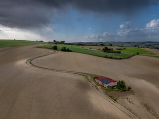 Italy, May 15, 2025: Aerial view of a farmhouse equipped with solar panels in the middle of plowed fields. Peace, tranquility with renewable energy is conveyed by this image
