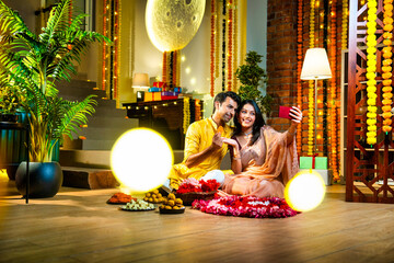 Calling friends with smartphone, cheerful Indian couple celebrates Diwali near flower rangoli