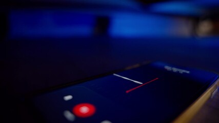 Smartphone screen with voice recorder application secretly grabbing conversation. Mobile phone hidden under bed or couch is covertly recording audio and sound for investigation surveillance evidence