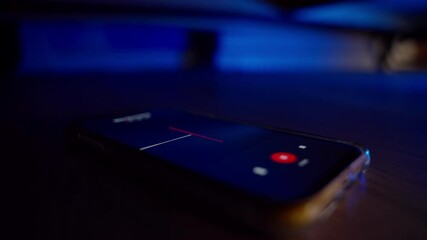 Voice recording app on phone captures conversation and audio in hidden spot. Under bed or couch mobile is secretly activated. Wiretapping suspect in criminal investigation or spy. Sound wave on screen