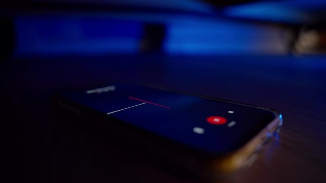 Voice recording app on phone captures conversation and audio in hidden spot. Under bed or couch mobile is secretly activated. Wiretapping suspect in criminal investigation or spy. Sound wave on screen