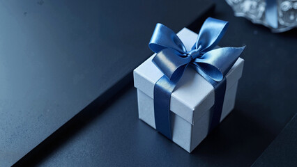 Elegant small luxury gift box with satin blue bow on dark table, high contrast monochrome, ideal for Father’s Day, Valentine’s Day, corporate gifting, or holiday promotions keywords: gift, box, 