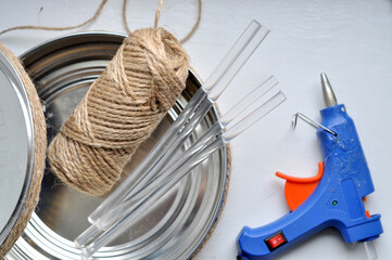 Close-up of DIY craft supplies including jute twine, metal lids, hot glue gun, and glue sticks....