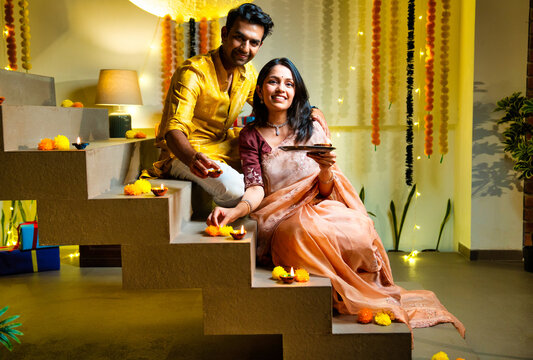 Placing diya on stair steps, Indian married couple celebrates Diwali wearing ethnic festive attire