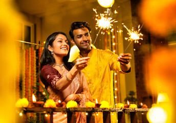 Young Indian couple enjoying festive night lighting sparklers and smiling during Diwali