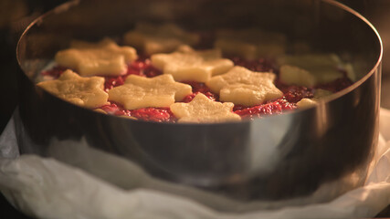 Raw raspberry pie with star-shaped shortcrust pastry on top baking in metal cake ring. Studio food photography. Holiday dessert preparation. Christmas baking concept for design and print