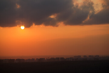 Sunset over city skyline with dark clouds. Urban landscape with orange sky and setting sun. Cityscape photography with copy space.