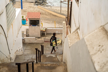 Fototapeta premium Surfer walking down stairs to beach with surfboard