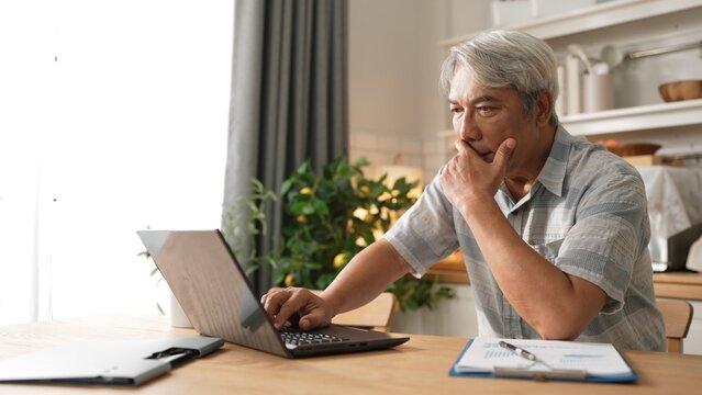 Stressful senior man looking at financial data and making decision. Elder business man working and using computer while planning digital marketing strategy and sitting at home. Problem. Myrmidon.