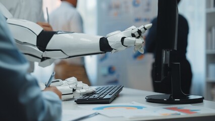 A robotic arm reaches towards a computer screen, symbolizing the integration of advanced technology in modern workplaces, enhancing efficiency and collaboration.Noogenesis