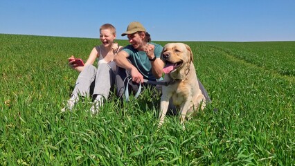 Two Friends Enjoy Relaxing Outdoors with a Dog in a Green Field