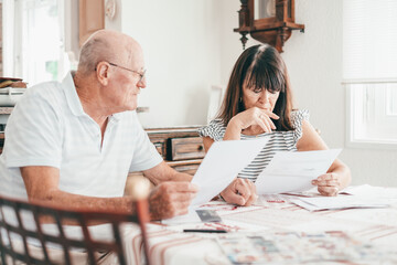 Senior couple sitting at home table with paper documents. Elderly man and woman reading documents, paying bills, managing bank finances, calculating taxes, planning loan, debt, insurance, pension