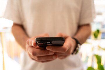 Close-up of man in white t-shirt typing message on mobile phone