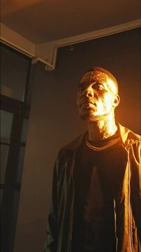 Rappeur illumin&eacute; par une lumi&egrave;re dor&eacute;e r&eacute;v&eacute;lant un visage craquel&eacute; fa&ccedil;on kintsugi

