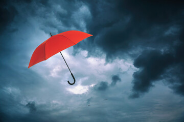 Red umbrella flying in dark cloudy sky. Stormy weather