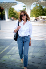 Full length of a blond haired woman wearing casual clothes and walking in city park